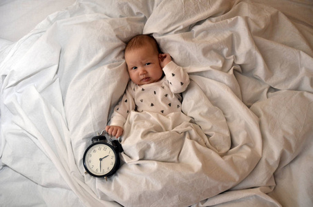 孩子躺在床上，一个闹钟和祝愿大家早上好。上班的时间。睡觉的时间。顶尖 viev