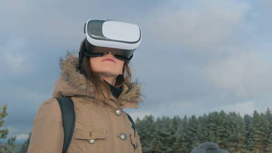 在冬季森林中使用虚拟现实的眼镜的女人