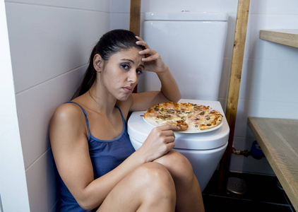 暴食女人觉得不舒服有罪坐在靠吃披萨的 wc 厕所地板照片