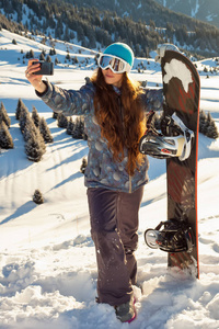 女孩的滑雪者站在山顶上日落和制作自拍照