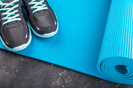 瑜伽垫和体育鞋在深色背景上。概念的健康生活方式 运动和饮食。运动器材。选择性的焦点