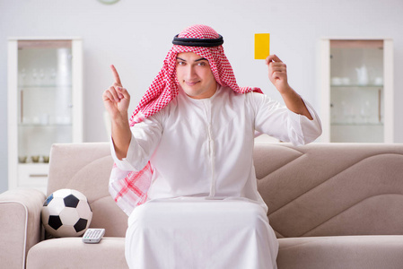 年轻的阿拉伯男人坐在沙发上看足球