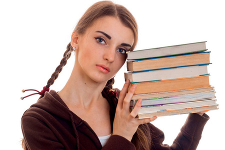 关闭了有吸引力的年轻学生女孩在棕色运动衣服用了很多书在白色背景上孤立的手中的画像