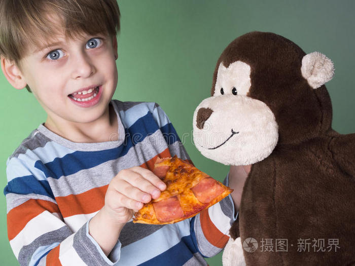 可爱的男孩用比萨饼喂他的猴子娃娃