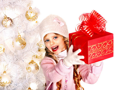 戴着帽子戴着手套的孩子，手里拿着白色圣诞树旁的红色礼品盒。