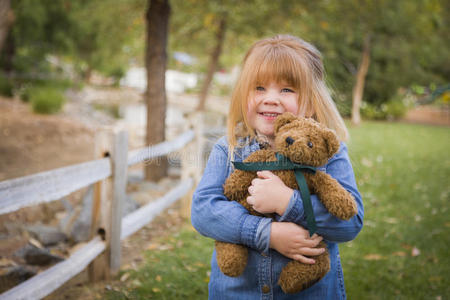 可爱微笑的小女孩在外面抱着她的泰迪熊