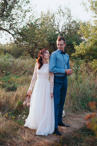 只是爱赶时髦的人夫妇的婚纱和西装在绿色的田野，在树林里