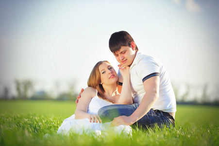 坐在绿草地上春天的年轻怀孕夫妇
