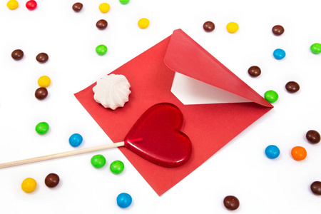 红包 酥皮和红色棒棒糖与多彩钮扣状的巧克力的白色背景上的一颗心的形状