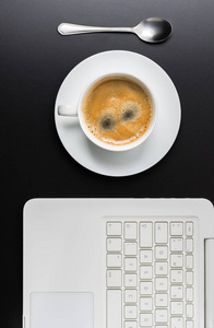 白杯咖啡与笔记本电脑的黑暗背景上。顶视图