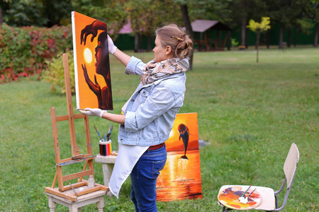 艺术家的女人握着绘画，看着它，在照相机摆姿势