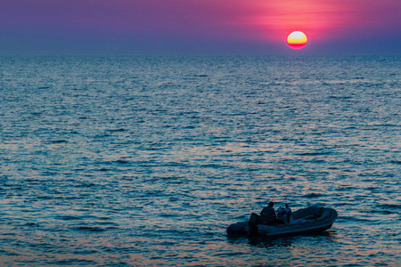 美丽的日落在海上与橙色，圆和明亮的太阳在黄昏在平静的海洋在戏剧性的天空背景。剪影船和不明身份的船司机在前景。卡马拉海滩景观
