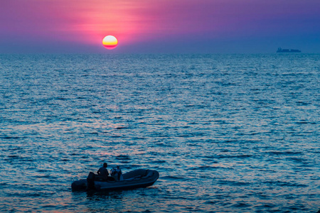 美丽的日落在海上与橙色，圆和明亮的太阳在黄昏在平静的海洋在戏剧性的天空背景。剪影船和不明身份的船司机在前景。卡马拉海滩景观