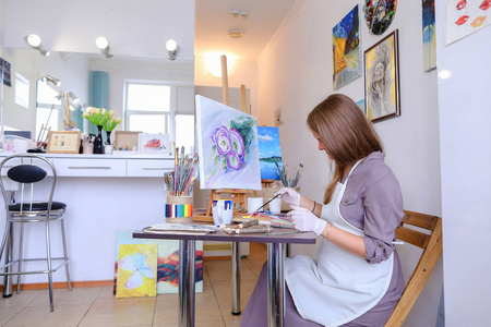 女孩坐在画架和写作绘画在凳子上，使用刷子