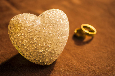 爱, 婚礼和情人节的概念。美丽的金色结婚戒指和玻璃心脏选择性的焦点。有用的贺卡黄色色调