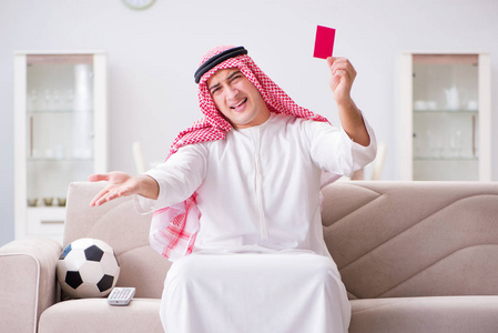年轻的阿拉伯男人坐在沙发上看足球