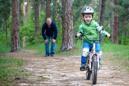 小小孩男孩 3 年和他的父亲在秋天的树林，用一辆自行车。爸爸教学的儿子。关于成功快乐的人。儿童头盔。安全 体育 休闲的孩子概