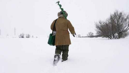 渔夫走在白雪覆盖的湖，寻找好的钓鱼的地方