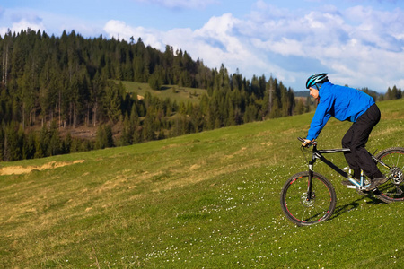 晴朗的日子，土路蜿蜒的绿色森林对蓝色的天空和美丽的云彩农村丘陵区骑山地自行车