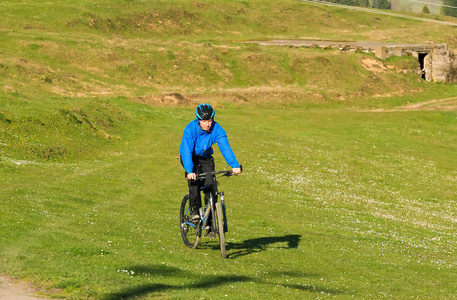 晴朗的日子，土路蜿蜒的绿色森林对蓝色的天空和美丽的云彩农村丘陵区骑山地自行车