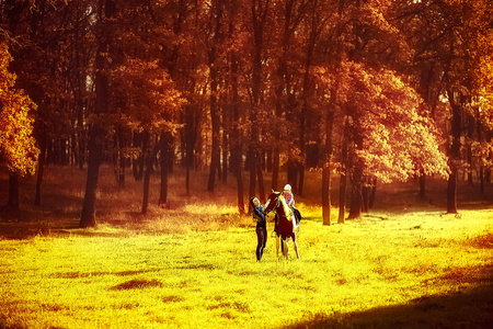 母亲带着女儿走在阳光明媚的草地和饲养一匹马