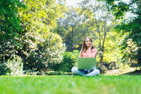 女学生使用一台笔记本电脑在一个绿色的公园
