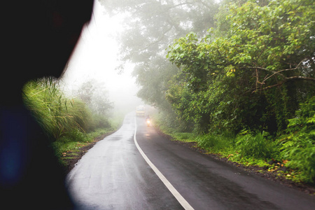 在路上，恶劣天气对驾驶摩托车的大雾。透过朦胧的常绿丛林森林的路。冬季多雨的季节。印度尼西亚