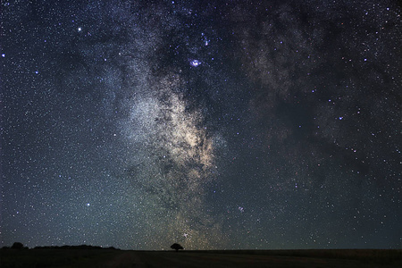 夜晚的风景与五颜六色的银河归档与孤独的树。 夏天有小山的星空。 美丽的宇宙。 空间背景