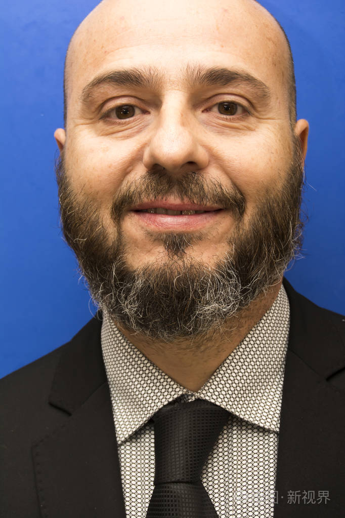 英俊秃顶男人留着胡子与西装和领带在蓝色的背景和目标