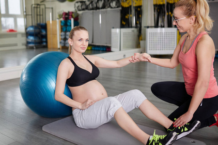 自信的怀孕女人，坐在与个人 tr 健身房垫上