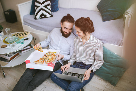 年轻的时髦男性女性夫妇家中吃披萨的笔记本电脑