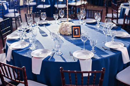 椅子和圆桌会议的客人,配餐具和陶器和蓝色的桌布盖着桌子中央的插花