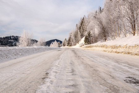 风景优美的冬天，从柏油路上看到白雪和美丽的树木，在霜冻的道路上，在群山蓝天和云彩的背景下。