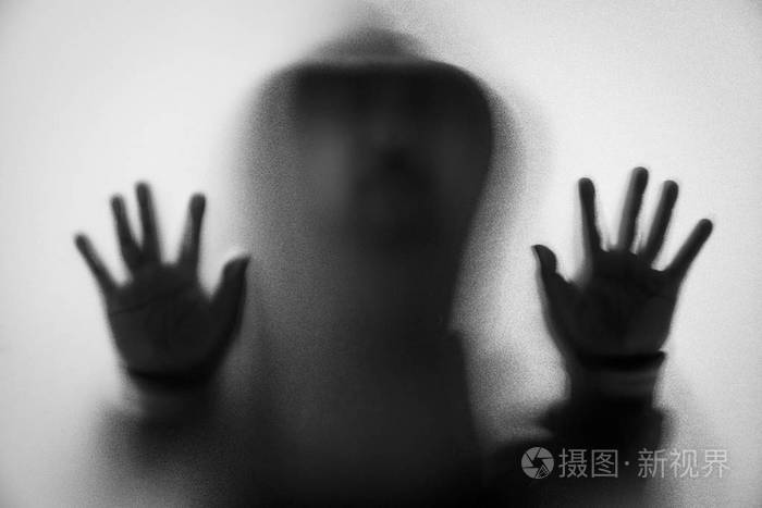 阴影模糊恐惧中的人带兜帽的夹克.在玻璃上的手