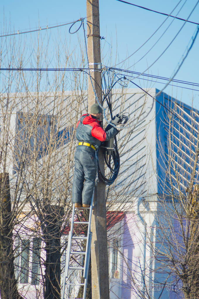 工人电工修理站在楼梯上的街道杆上的电线