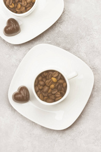 白色杯子里的咖啡充满咖啡豆和巧克力心光背景上的形式。顶视图。色调