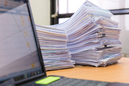 笔记本电脑和桌上的文件堆高等待照片