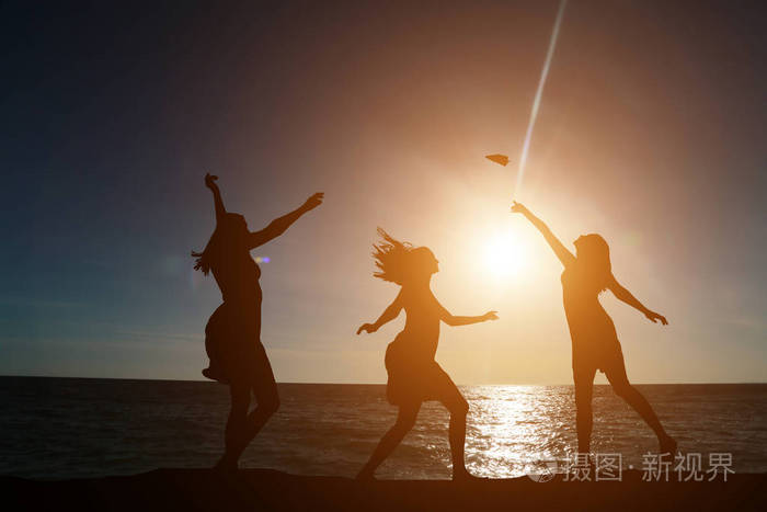 三个女孩在美丽的日落和大海的背景下在剪影中跳舞
