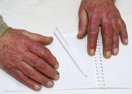 一个拿着笔和纸的老白种人皱巴巴的手特写镜头照片