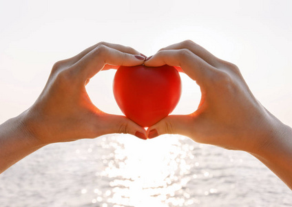 手的女性在夏季海在落日的天空举起红色的心照片