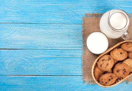 壶和杯牛奶燕麦饼干上蓝色的木制背景与副本空间为您的文本。顶视图