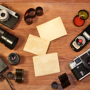 老式照片相机和其他旧复古摄影配件的顶部视图在木制桌板上，有一些清晰的白色空白相框，以放置您的图片或文本。