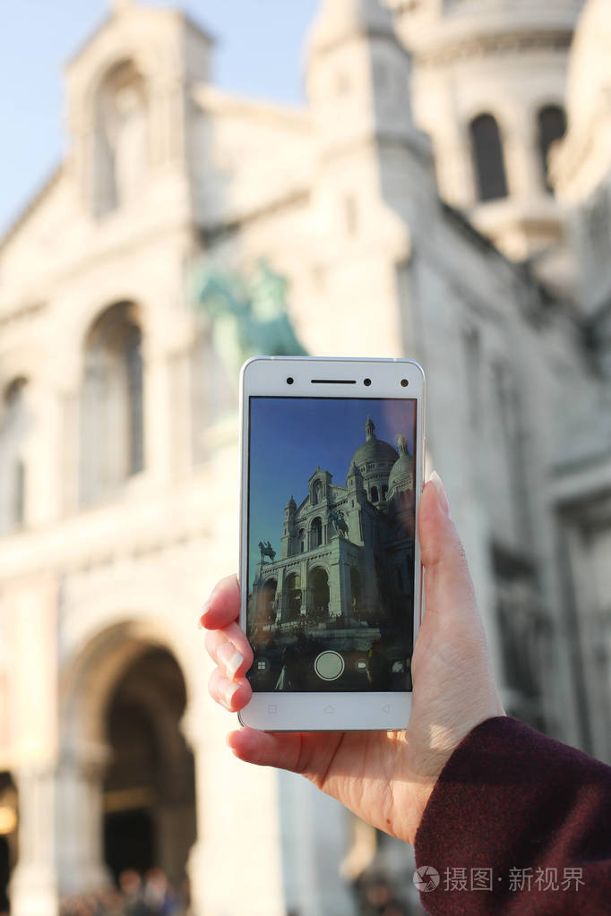 在巴黎的女人正在拍照的圣心大教堂与她的移动电话