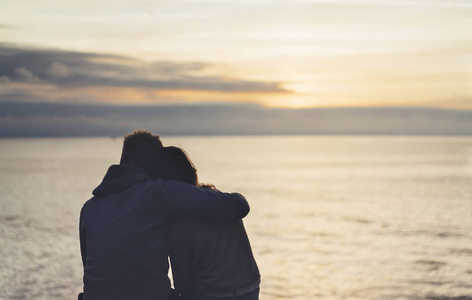 夫妇在背景海洋日出在沙滩上拥抱,两个浪漫的人的侧影拥抱,看后视晚上