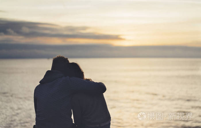 夫妇在背景海洋日出在沙滩上拥抱两个浪漫的人的侧影拥抱看后视晚上