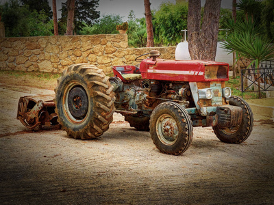 老时尚仿古磨损生锈农村红四轮拖拉机绿树之间。老农业产业机履带拖拉机农用车辆。抽象的农用拖拉机生锈的金属兽