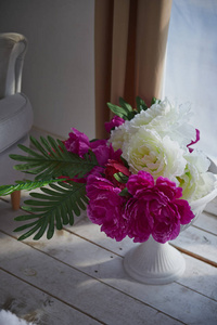 在明亮的房间里, 在木地板上放置了花瓶和白色及紫色蓬松的牡丹