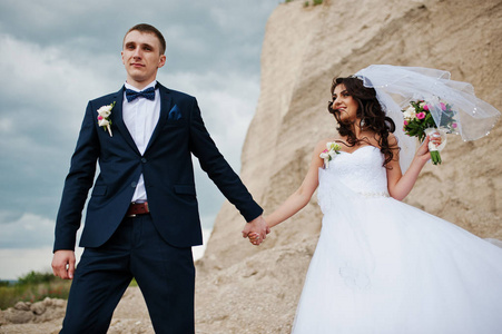 年轻时尚的婚礼夫妇对沙地的事业，在多云的天空