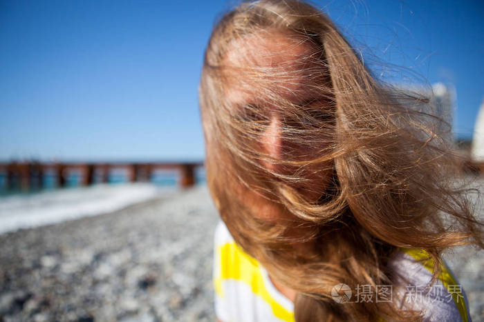 年轻漂亮的女孩在夏天阳光明媚的日子在海边的街道上强风吹乱了发型