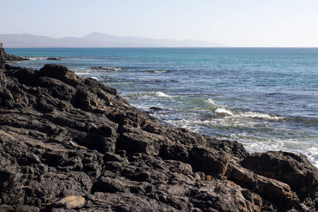 黑色的岩石的卡尔玛海滩。蓝色的海岸线。普拉亚巴萨，西班牙加那利群岛富埃特文图拉。凼连贯公路德拉削视图
